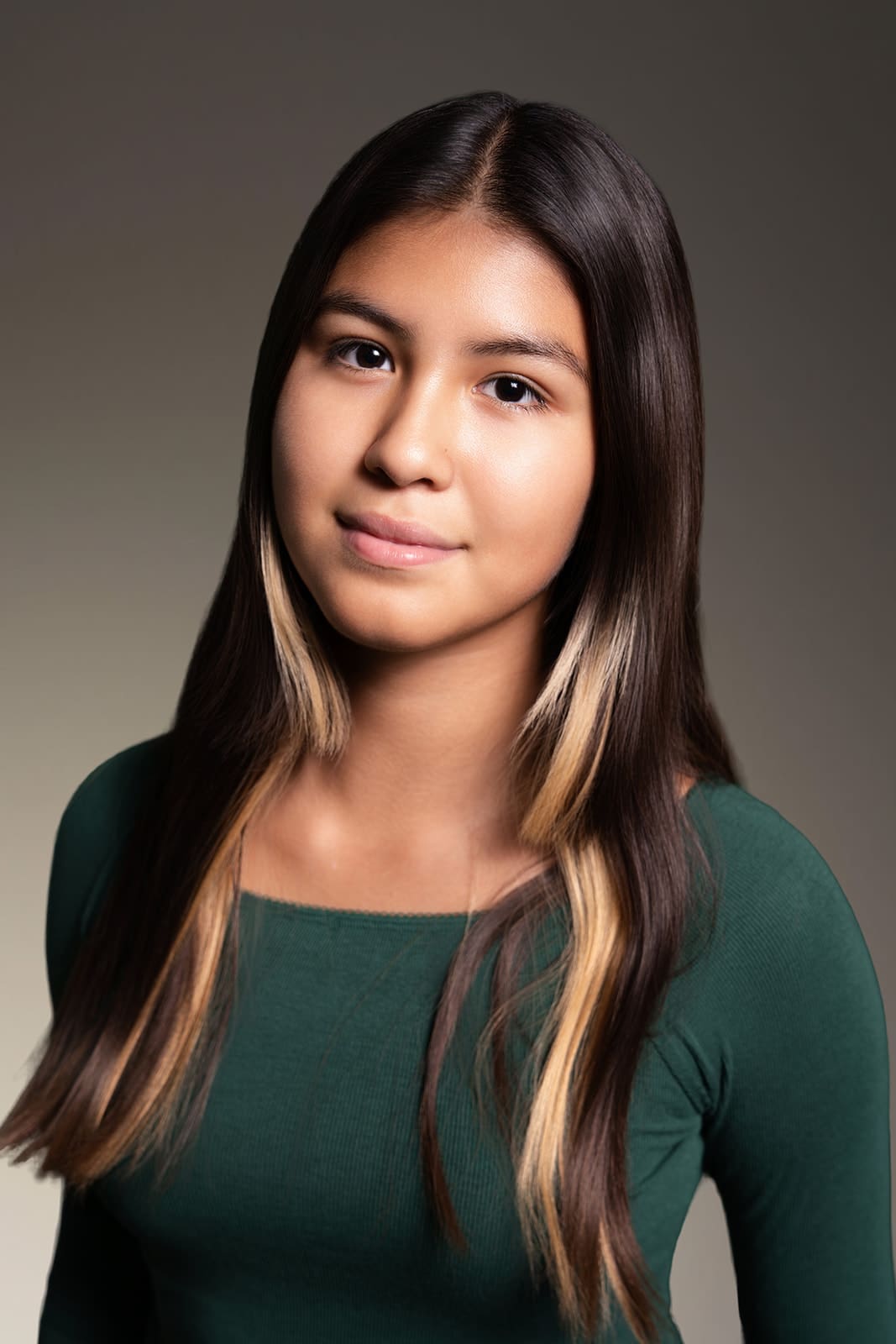 Abigail smiling softly in a green top, photographed in Minneapolis studio lighting for professional kids modeling headshots by Dahli Durley.