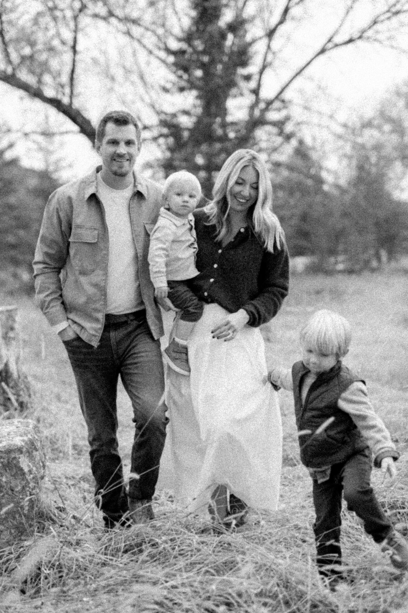 Family walking outdoors through tall grass during a fall session in Hokah, Minnesota, captured candidly by photographer Dahli Durley in soft, nostalgic black-and-white film style.