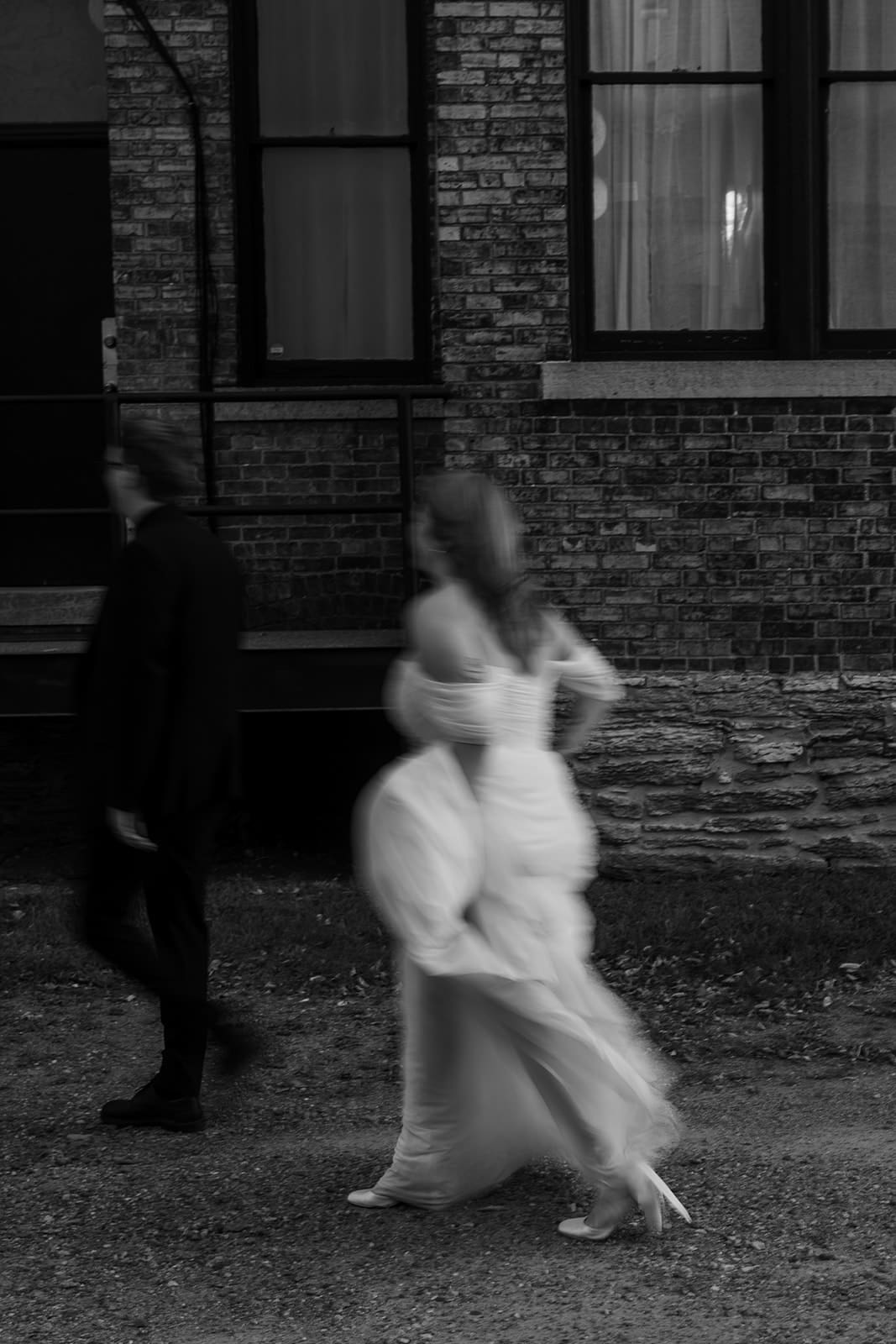 Maura and Isaiah walking together after their intimate Minneapolis wedding, captured in soft motion against a brick wall for a cinematic, documentary-style photo by Dahli Durley.