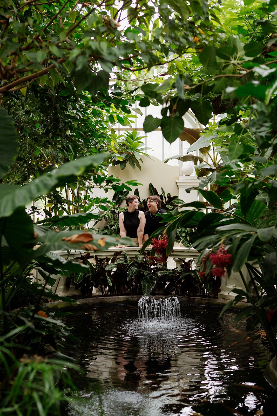 Mitch and Mari enjoying their Como Conservatory engagement photos surrounded by lush green plants and a quiet indoor pond.