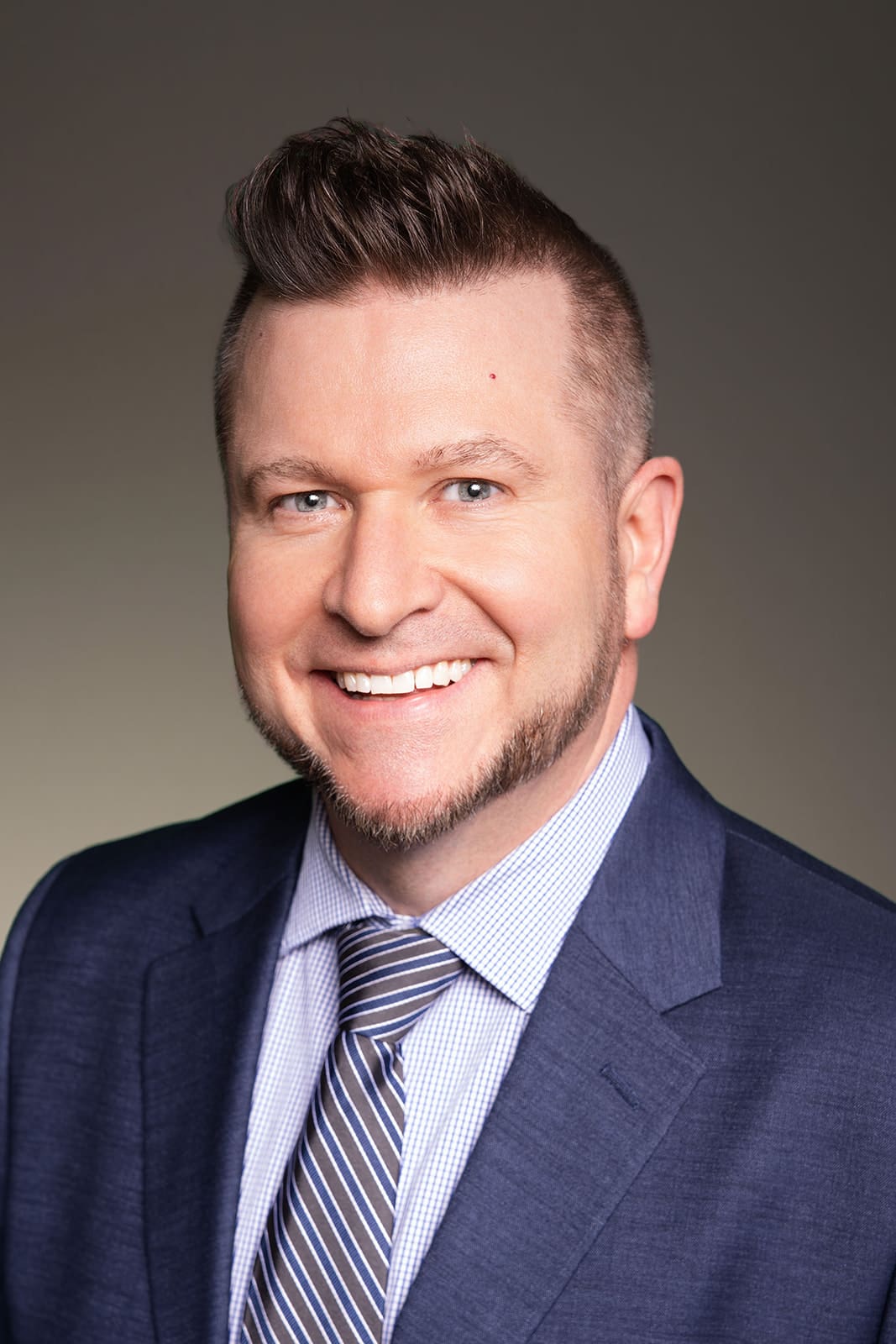 Peter Peterson smiling in a blue suit and striped tie, photographed in Minneapolis studio lighting for professional modeling and agency headshots by Dahli Durley.
