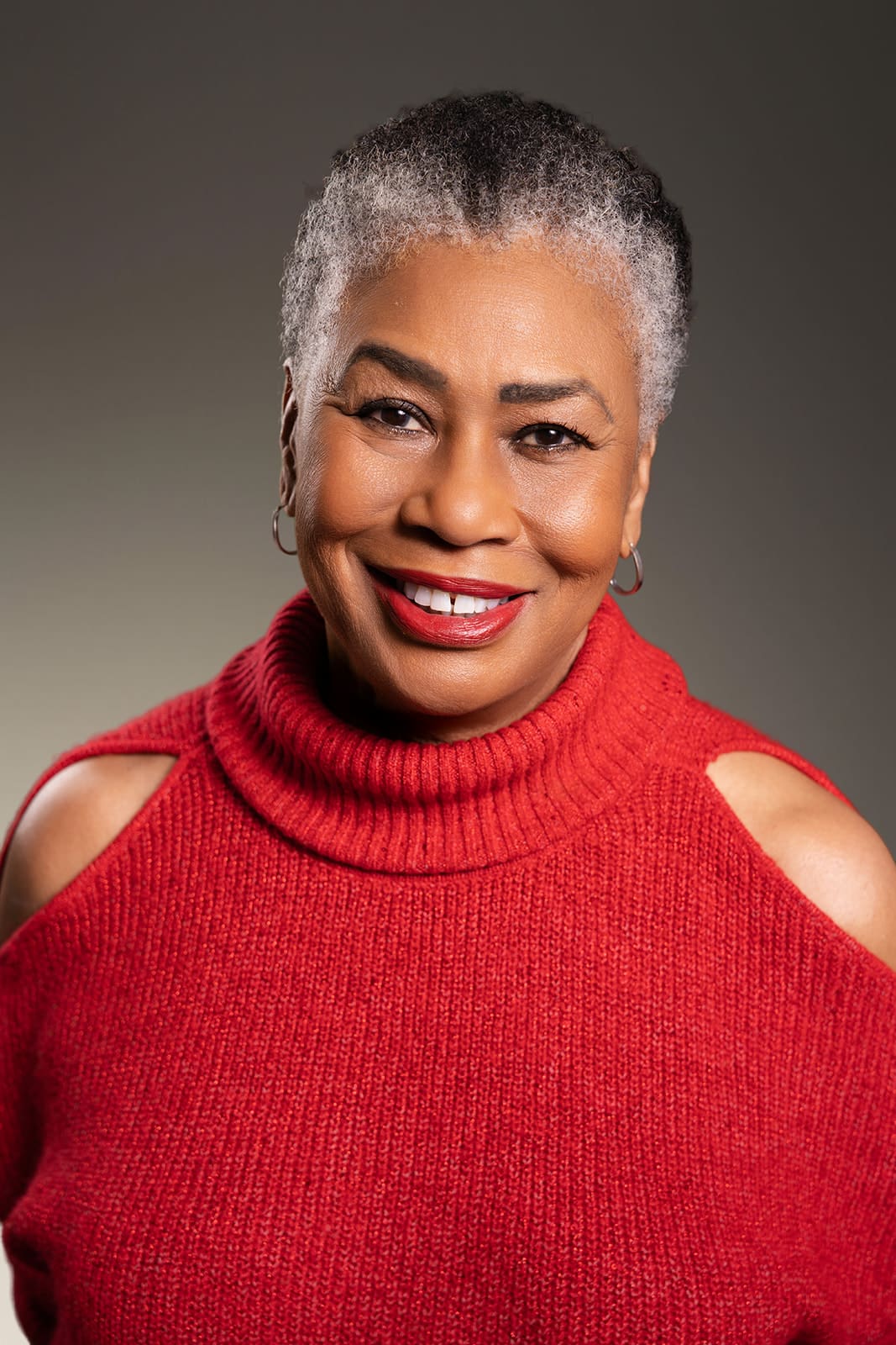 Portrait of Sylvia smiling in a red sweater, photographed in Minneapolis studio lighting for professional modeling and commercial headshots by Dahli Durley.